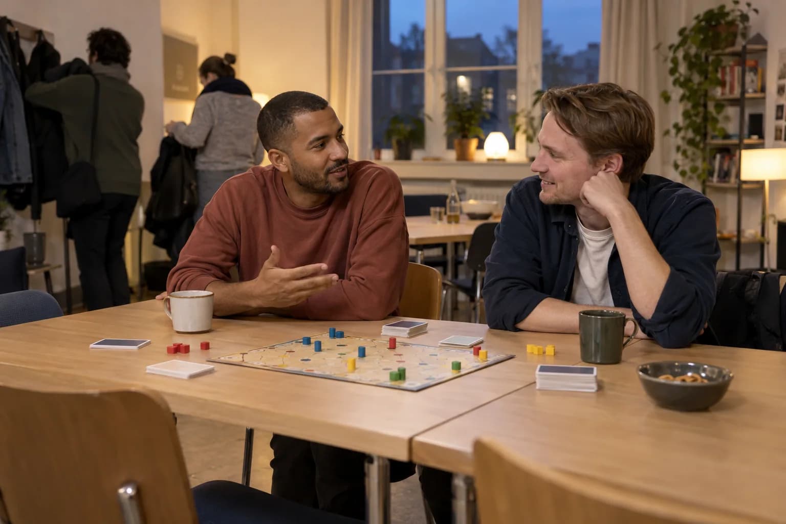 Two men talk beside a board game at a community games evening.