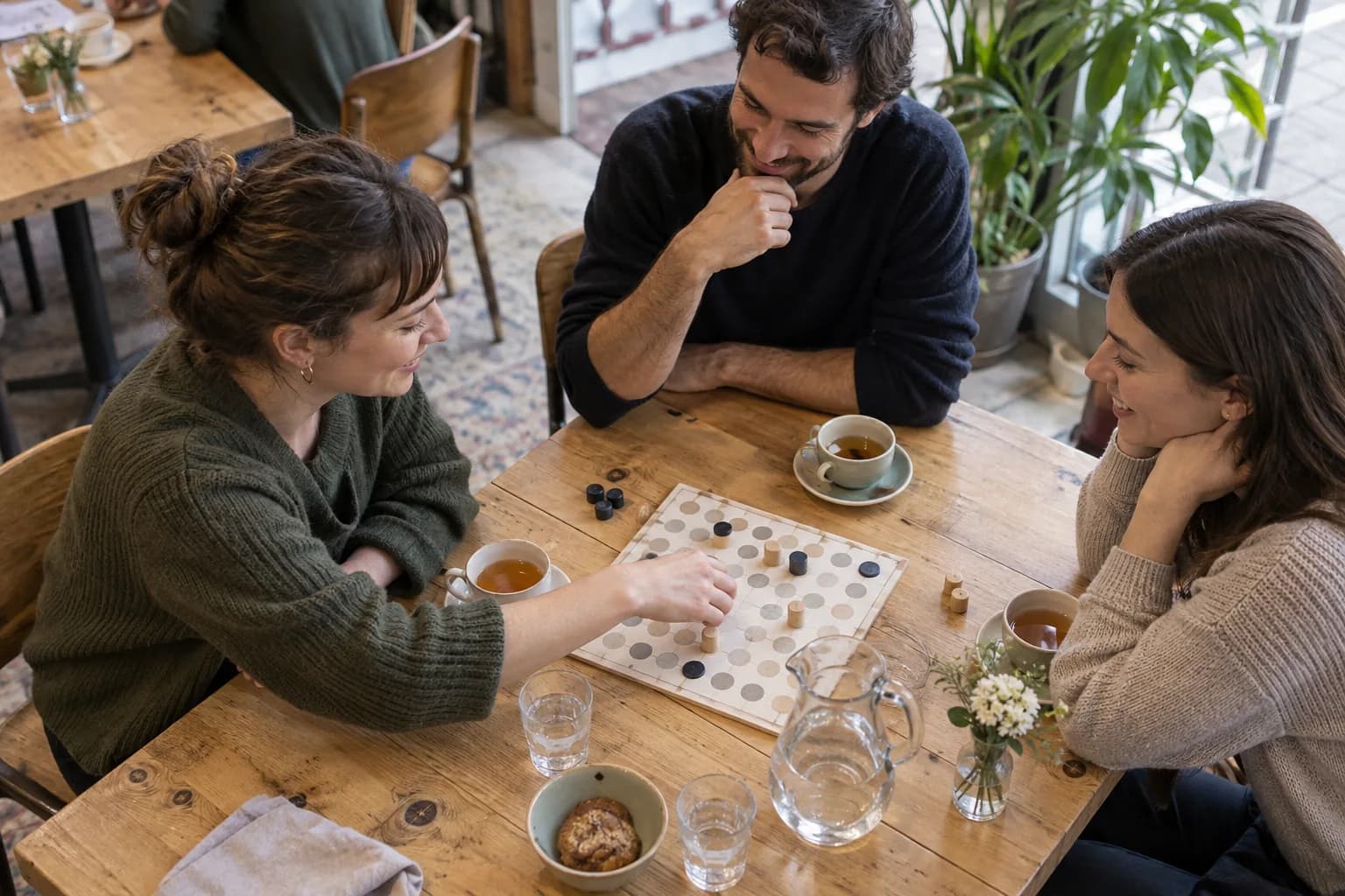 Three adults play a board game with tea and water on the table.